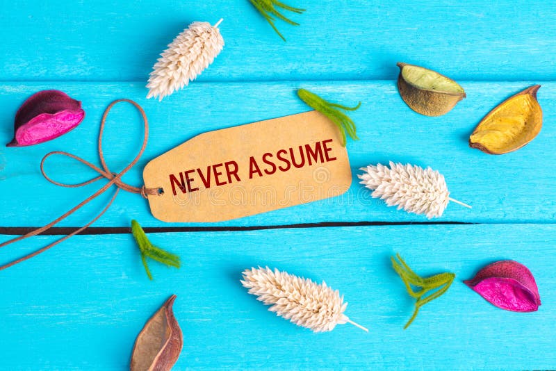 Never assume text on paper tag with rope and color dried flowers around on blue wooden background. Never assume text on paper tag with rope and color dried flowers around on blue wooden background