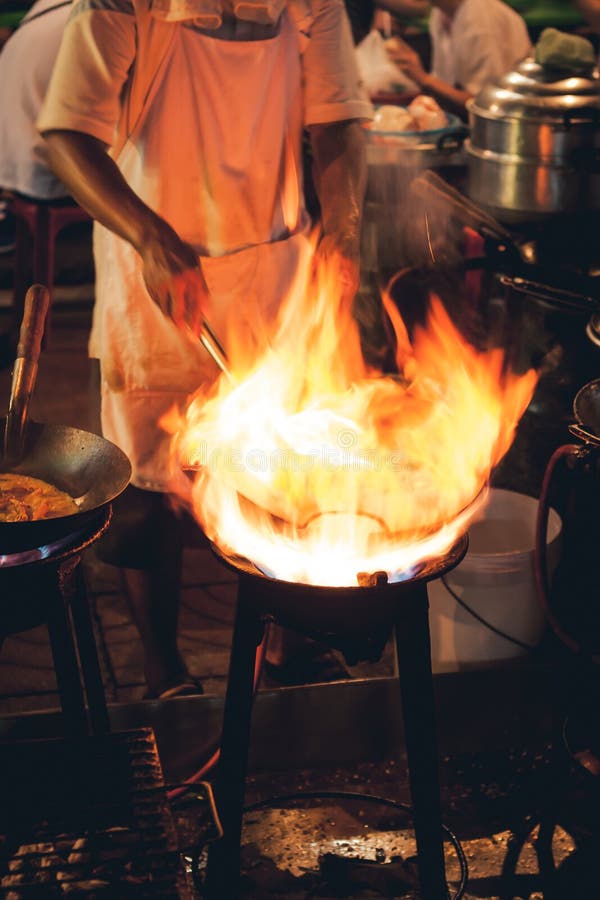 Street food chef cooking meat and fish in a pan with fire and flames under it. Chinatown, Bangkok, Thailand