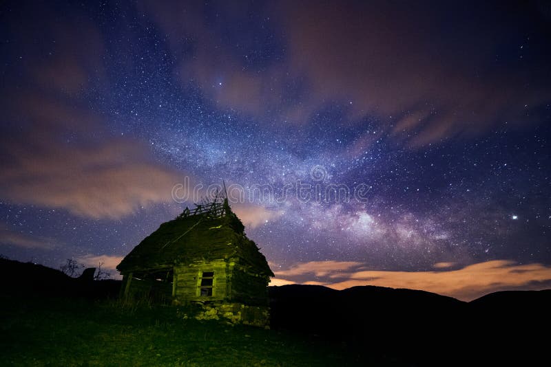 Night sky full of stars with some clouds and the milky way galaxy and an old rustic barn house in the foreground