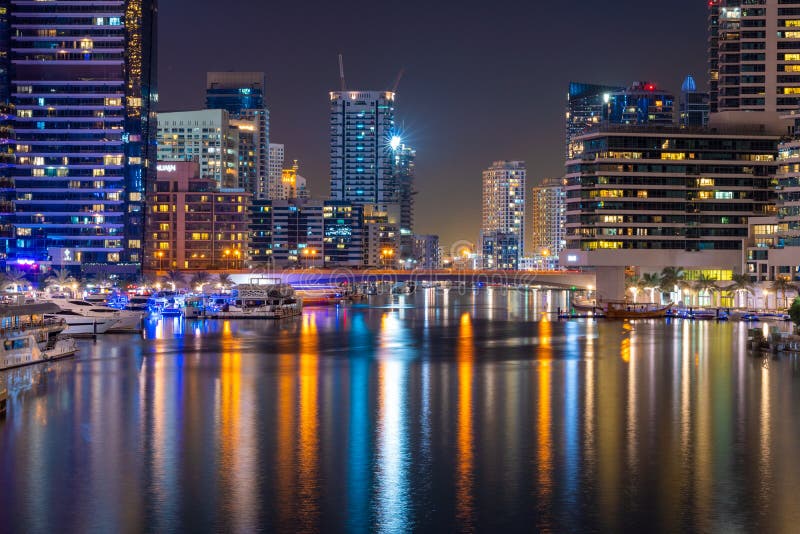 Night view to Dubai Marina panorama, reveals skyscrapers and beautiful bridge. Amazing colors reflect on the water. Luxury destina