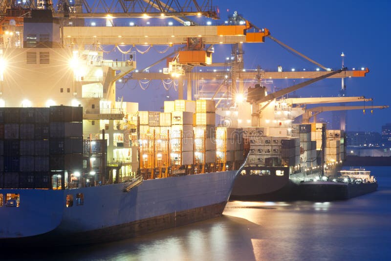 Nightly harbor activity. Two container ships being unloaded at the Rotterdam Harbor. A small support vessel is moored off next to the freight carrier in front royalty free stock photos Nightly harbor activity. Two container ships being unloaded at the Rotterdam Harbor. A small support vessel is moored off next to the freight carrier in front royalty free stock photos