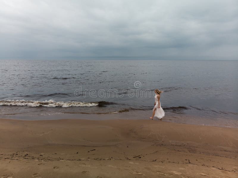 Ninfa rubia joven hermosa a?rea de la playa de la mujer en el vestido blanco cerca del mar con las ondas durante un tiempo melanc fotos de archivo Ninfa rubia joven hermosa a?rea de la playa de la mujer en el vestido blanco cerca del mar con las ondas durante un tiempo melanc fotos de archivo