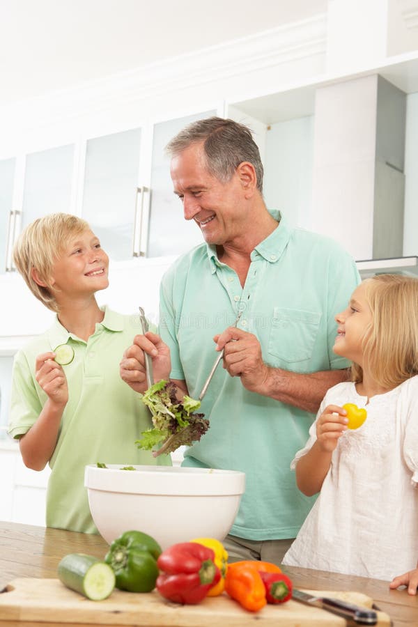 Nipoti che aiutano nonno a preparare insalata immagine stock Nipoti che aiutano nonno a preparare insalata immagine stock