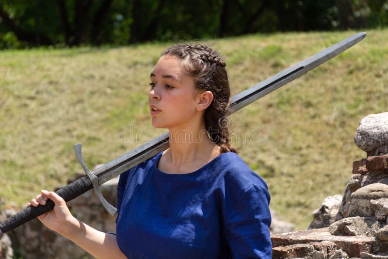 Portrait of a medieval lady in a blue dress holding a big sword on the shoulder royalty free stock photo Portrait of a medieval lady in a blue dress holding a big sword on the shoulder royalty free stock photo