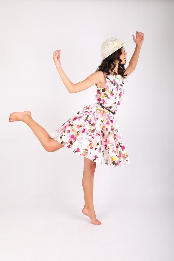 Pretty teenage girl - barefoot schoolkid with brunette hair dressed in nice light summer dress and white hat dancing on white background. Portrait photography concept. Pretty teenage girl - barefoot schoolkid with brunette hair dressed in nice light summer dress and white hat dancing on white background. Portrait photography concept.