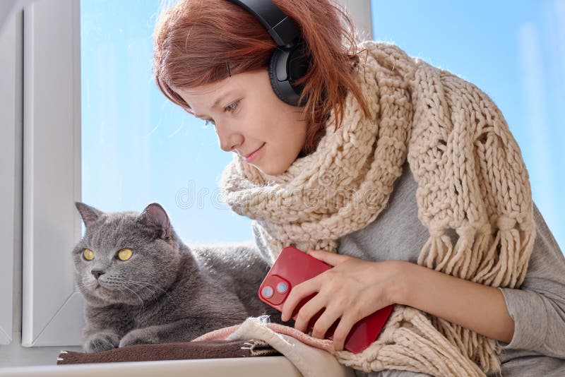 Niña adolescente con pañuelo de madera de punto con gato cerca de la ventana de invierno fotos de archivo libres de regalías