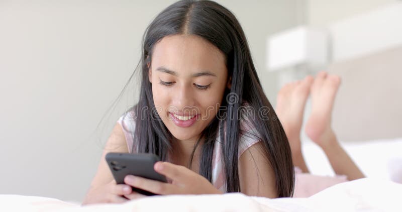 Niña adolescente que está en la cama usando un smartphone y sonriendo disfrutando del tiempo libre almacen de metraje de vídeo