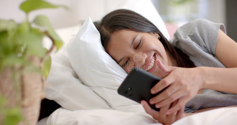 Niña adolescente que vive en la cama sonriendo mientras usa un smartphone disfrutando del tiempo libre metrajes