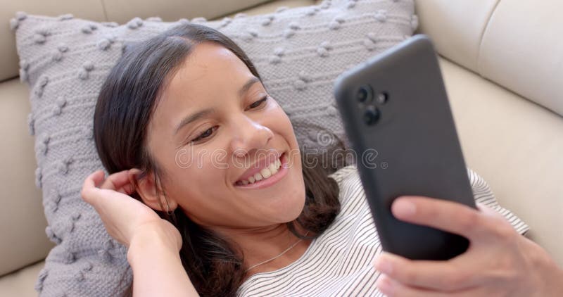 Niña adolescente sonriente tendida en el sofá usando un smartphone para videollamada metrajes