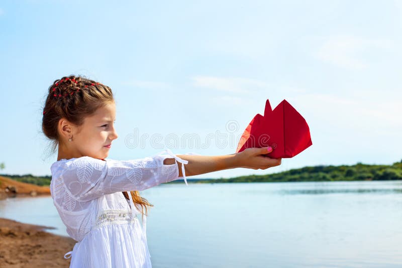 Niña adorable que sostiene el barco de papel rojo fotografía de archivo