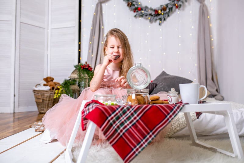 Niña bonita 4 años en un vestido rosado Niño en el cuarto de la Navidad con una cama, comiendo el caramelo, el chocolate, las gal fotos de archivo Niña bonita 4 años en un vestido rosado Niño en el cuarto de la Navidad con una cama, comiendo el caramelo, el chocolate, las gal fotos de archivo