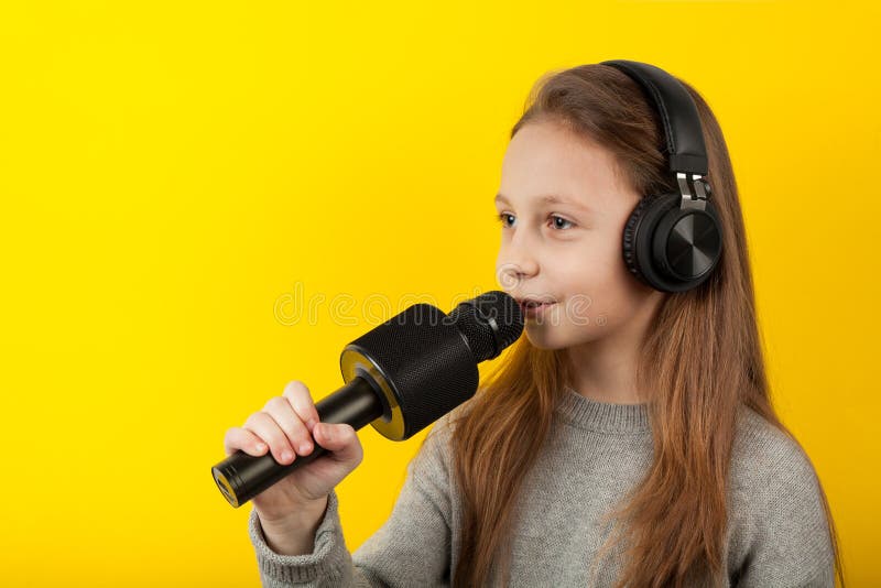Niña canta en un micrófono con un fondo amarillo Karaoke para los niños imagenes de archivo Niña canta en un micrófono con un fondo amarillo Karaoke para los niños imagenes de archivo