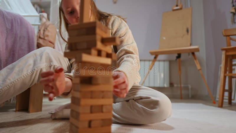 Niña caucásica con suéter beige y jeans está construyendo una torre a partir de pequeños bloques de madera almacen de metraje de vídeo