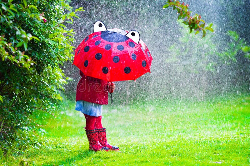 Niña con el paraguas que juega en la lluvia