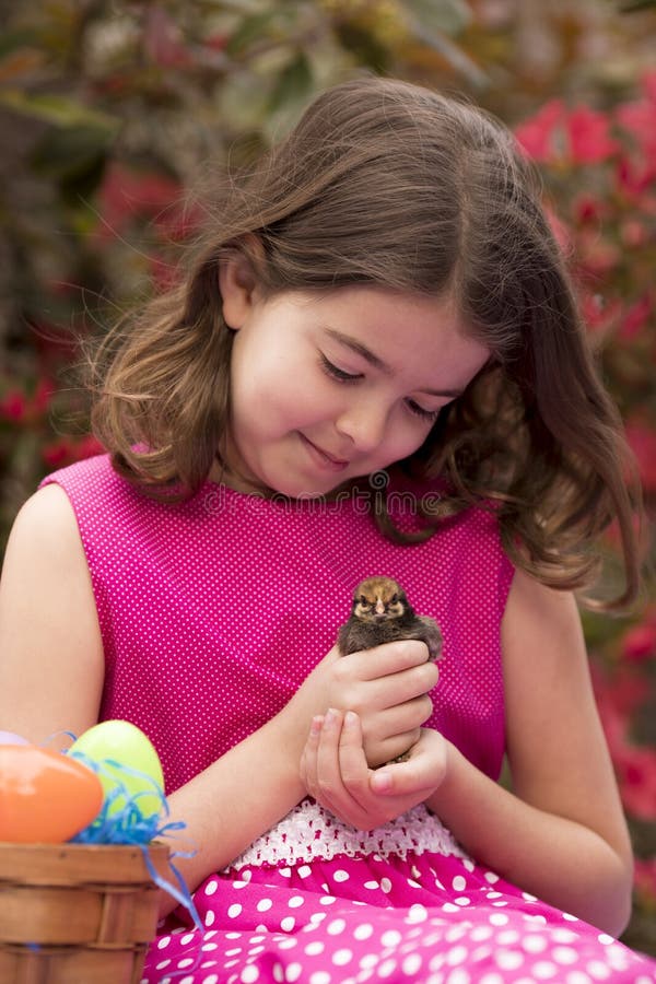 Niña con la cesta de pascua que juega con el polluelo del bebé