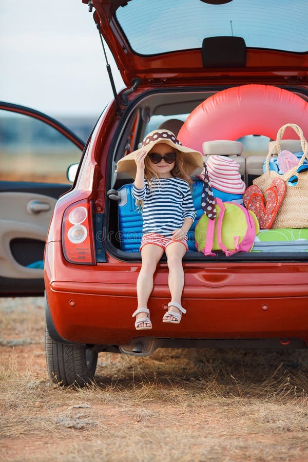 Niña en el sombrero de paja que se sienta en el tronco de un coche foto de archivo Niña en el sombrero de paja que se sienta en el tronco de un coche foto de archivo