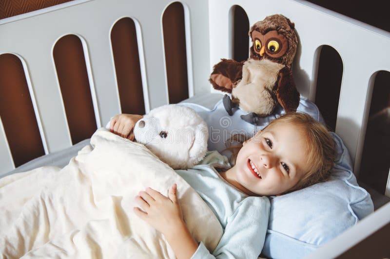 Niña en la hora de acostarse con los juguetes en cama foto de archivo Niña en la hora de acostarse con los juguetes en cama foto de archivo