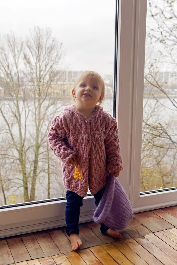 Little girl in a purple sweater and cap standing at the window. Little girl in a purple sweater and cap standing at the window