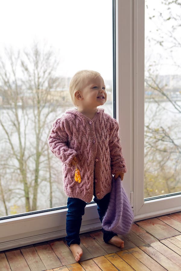 Little girl in a purple sweater and cap standing at the window. Little girl in a purple sweater and cap standing at the window
