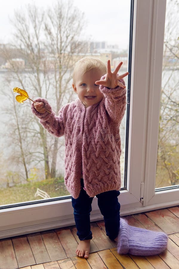 Little girl in a purple sweater and cap standing at the window. Little girl in a purple sweater and cap standing at the window