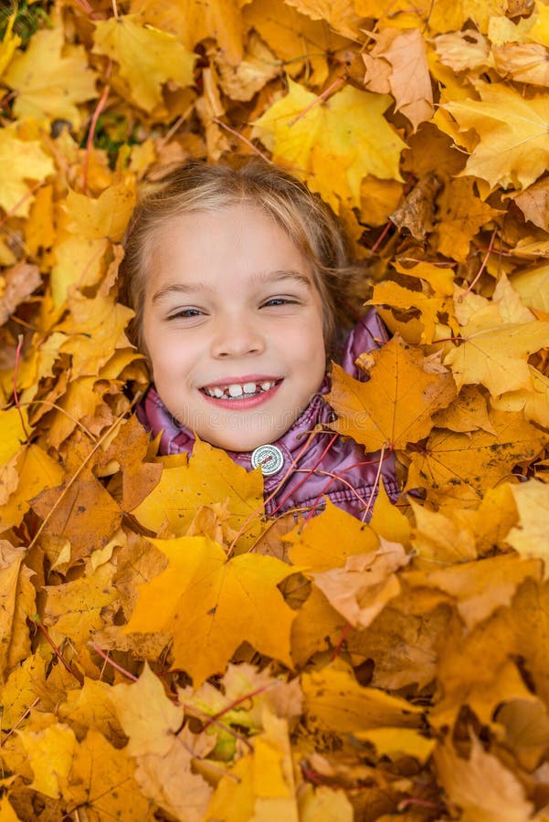 Niña enterrada en amarillo de las hojas de otoño foto de archivo libre de regalías Niña enterrada en amarillo de las hojas de otoño foto de archivo libre de regalías