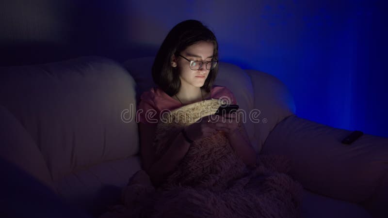 Niña feliz sentada frente a la tv por la noche y usando el teléfono