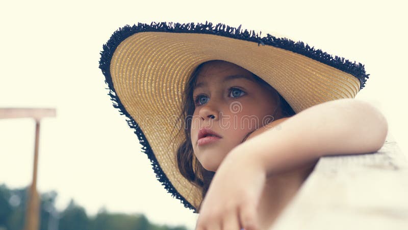Niña hermosa en un sombrero que se sienta en las escaleras que llevan al mar y a las miradas hacia fuera en la distancia foto de archivo libre de regalías Niña hermosa en un sombrero que se sienta en las escaleras que llevan al mar y a las miradas hacia fuera en la distancia foto de archivo libre de regalías