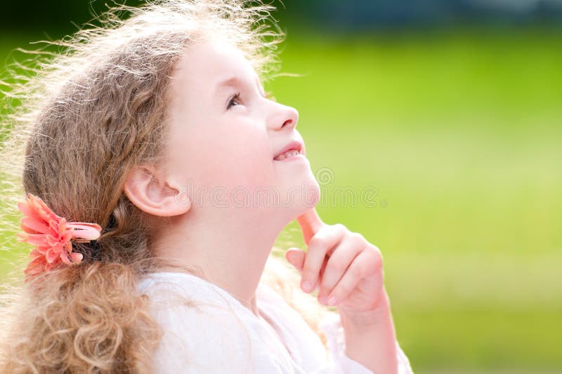 Beautiful little and happy girl smiling and looking up, hand under her chin. Summer park in background. Beautiful little and happy girl smiling and looking up, hand under her chin. Summer park in background.