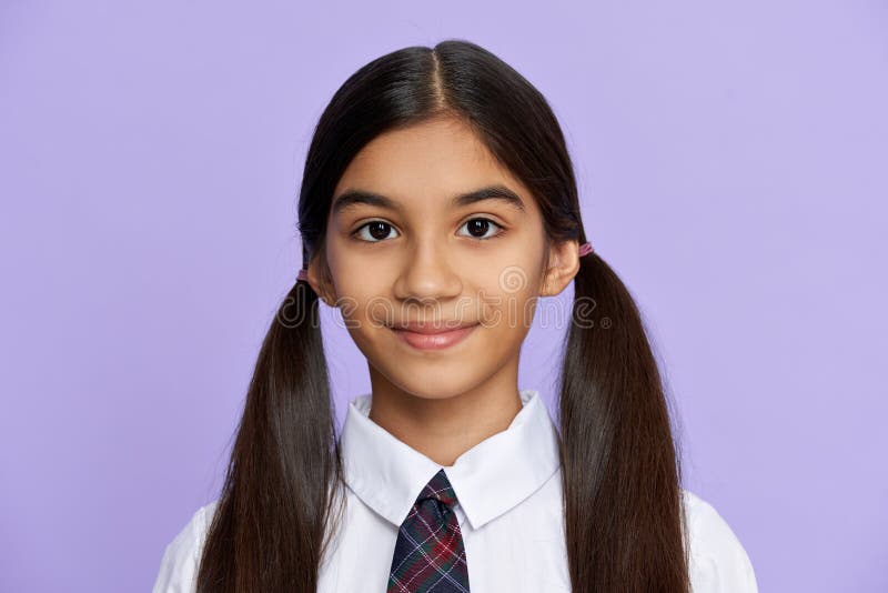 Cute pretty smiling indian hispanic tween kid girl with ponytails wearing school uniform standing isolated on lilac violet background. Latin schoolgirl looking at camera, headshot close up portrait. Cute pretty smiling indian hispanic tween kid girl with ponytails wearing school uniform standing isolated on lilac violet background. Latin schoolgirl looking at camera, headshot close up portrait.