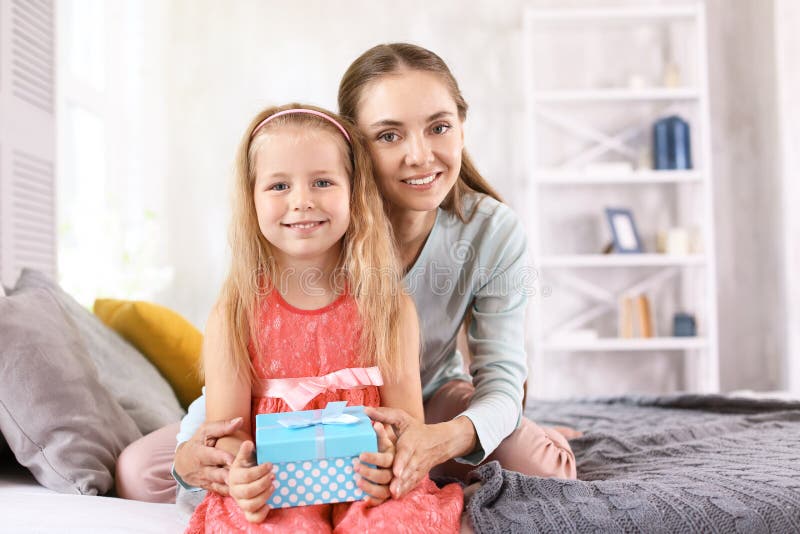 Niña linda con su caja de la mamá y de regalo que se sienta en cama en casa fotografía de archivo libre de regalías Niña linda con su caja de la mamá y de regalo que se sienta en cama en casa fotografía de archivo libre de regalías
