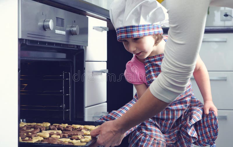 Niña linda con sus galletas de la hornada de la madre en horno imagenes de archivo Niña linda con sus galletas de la hornada de la madre en horno imagenes de archivo