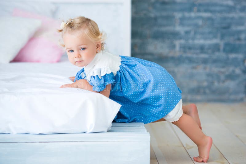 Niña linda en el vestido azul que miente en la cama en el interior Hora de acostarse imagen de archivo libre de regalías Niña linda en el vestido azul que miente en la cama en el interior Hora de acostarse imagen de archivo libre de regalías