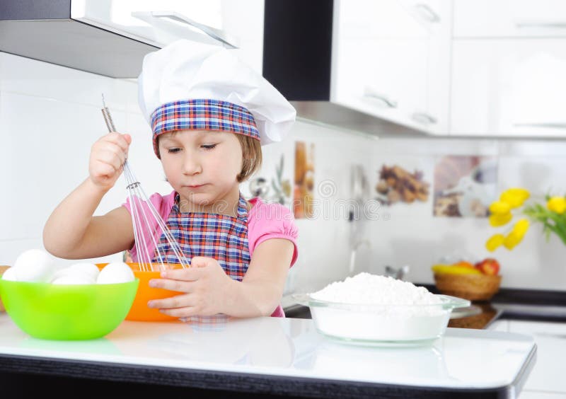 Niña linda en delantal que bate los huevos foto de archivo Niña linda en delantal que bate los huevos foto de archivo