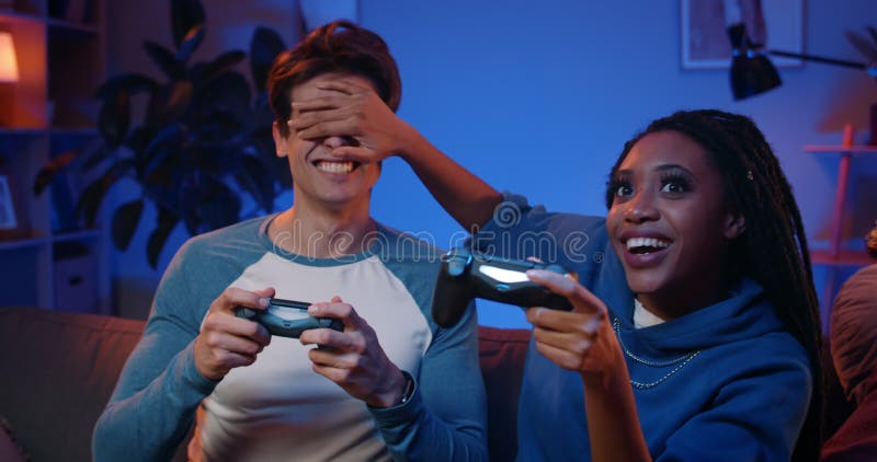 Niña milenaria cubriendo los ojos de su novio apuesto mientras jugaba videojuegos en casa. el tipo está abrazando a su novia almacen de video