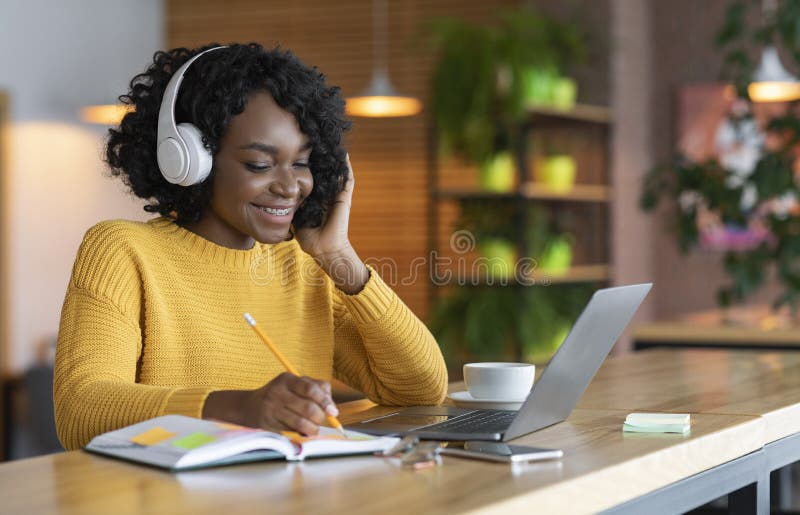 Niña negra con auriculares estudiando en línea, usando laptop en el café