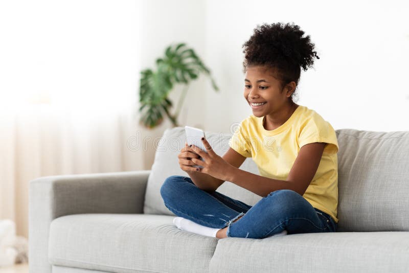 Niña negra jugando en línea con un smartphone sentada en casa imagen de archivo libre de regalías