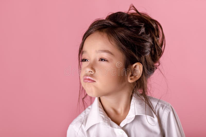 Niña orgullosa linda en la camisa blanca en fondo rosado Emociones humanas y expresión facial imagen de archivo