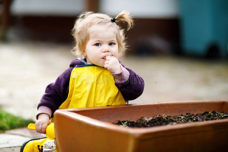 Niña pequeña adorable linda que juega con la arena y la pala el día de primavera El niño del bebé que lleva botas amarillas y el fotos de archivo Niña pequeña adorable linda que juega con la arena y la pala el día de primavera El niño del bebé que lleva botas amarillas y el fotos de archivo