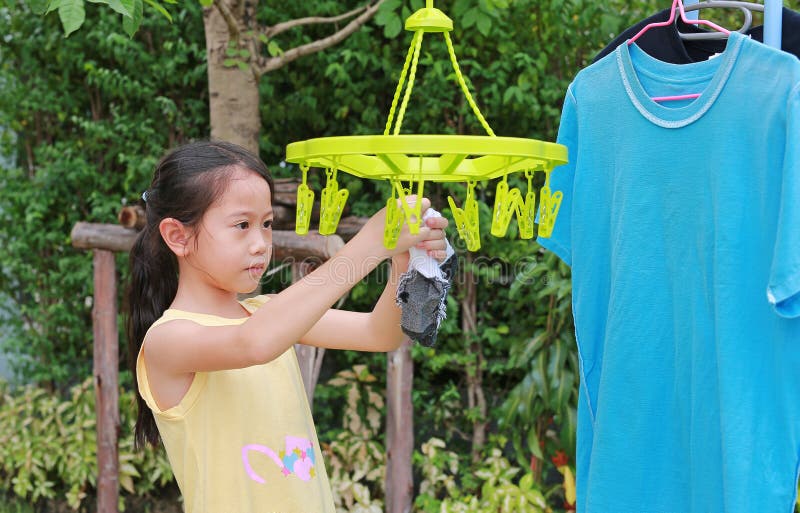 Asian little child girl putting clothespin and hangs socks to dry a clothes. Kid doing laundry in the garden. Asian little child girl putting clothespin and hangs socks to dry a clothes. Kid doing laundry in the garden.