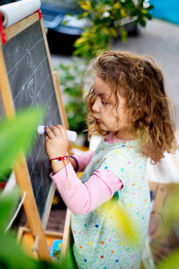 Niña pequeña dibujando a una persona en una pizarra. niños que disfrutan de un proceso de aprendizaje lúdico. Niña pequeña dibujando a una persona en una pizarra con tiza al aire libre. educación escolar. volver a la escuela.