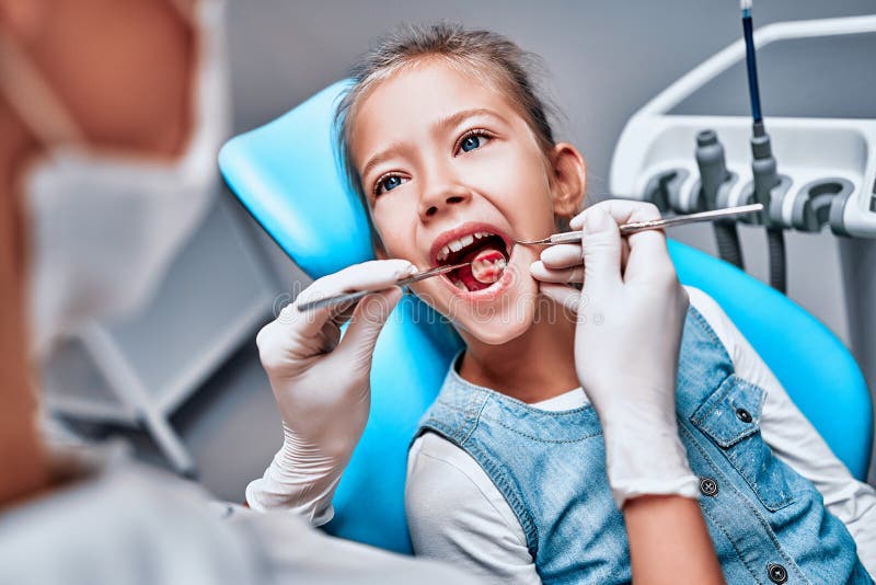 Niña pequeña sentada en una silla dental con la boca abierta y que siente miedo durante el chequeo oral mientras es médico foto de archivo libre de regalías Niña pequeña sentada en una silla dental con la boca abierta y que siente miedo durante el chequeo oral mientras es médico foto de archivo libre de regalías