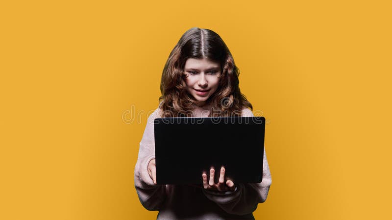 Niña preadolescente mirando en un portátil con fondo amarillo fotografía de archivo libre de regalías