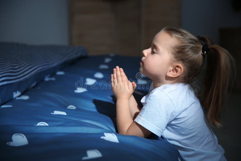 Niña que dice rezo de la hora de acostarse cerca de cama en sitio imagen de archivo libre de regalías Niña que dice rezo de la hora de acostarse cerca de cama en sitio imagen de archivo libre de regalías