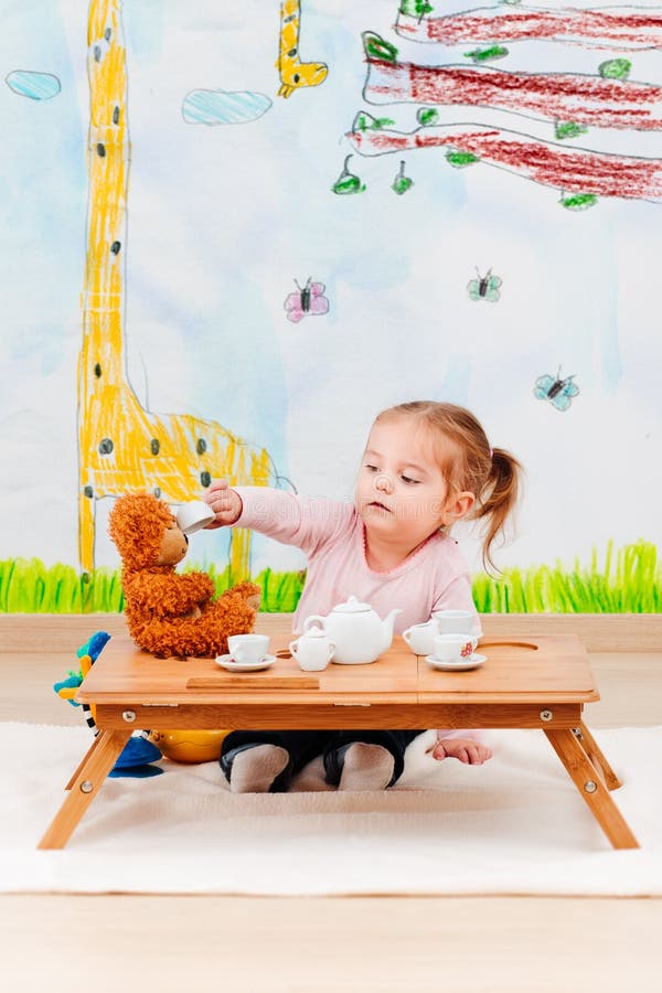 Niña que juega con su oso de peluche en la fiesta del té imagen de archivo Niña que juega con su oso de peluche en la fiesta del té imagen de archivo