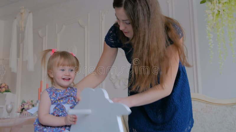 Niña que juega en caballo mecedora de madera