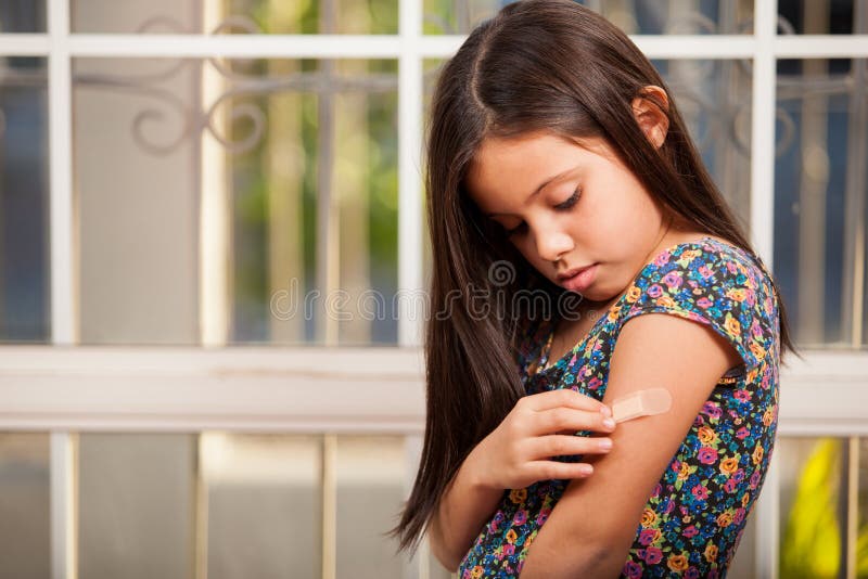 Niña que pone una tirita foto de archivo Niña que pone una tirita foto de archivo