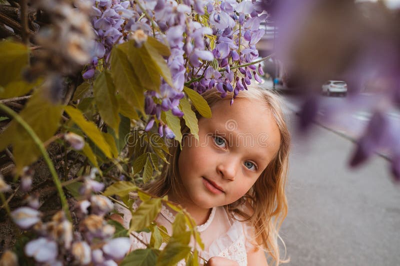 Niña sonriendo entre las flores de glicinia morada fotos de archivo