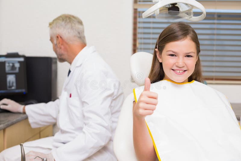 Smiling little girl showing thumbs up in dentists chair at the dental clinic. Smiling little girl showing thumbs up in dentists chair at the dental clinic