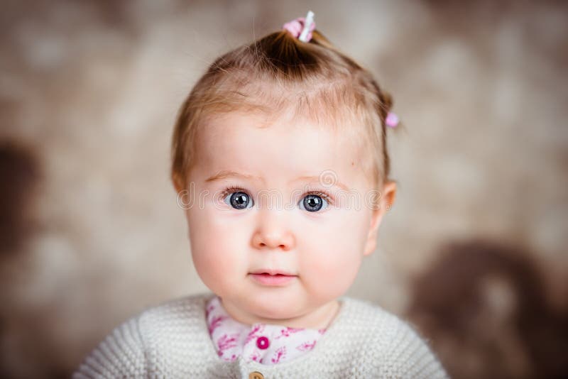 Amazed little girl with big grey eyes and plump cheeks. Close-up studio portrait on brown grunge background. Amazed little girl with big grey eyes and plump cheeks. Close-up studio portrait on brown grunge background