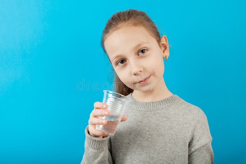 Niña sujeta en la mano agua mineral pura de vidrio, retrato de fondo azul imagen de archivo libre de regalías Niña sujeta en la mano agua mineral pura de vidrio, retrato de fondo azul imagen de archivo libre de regalías